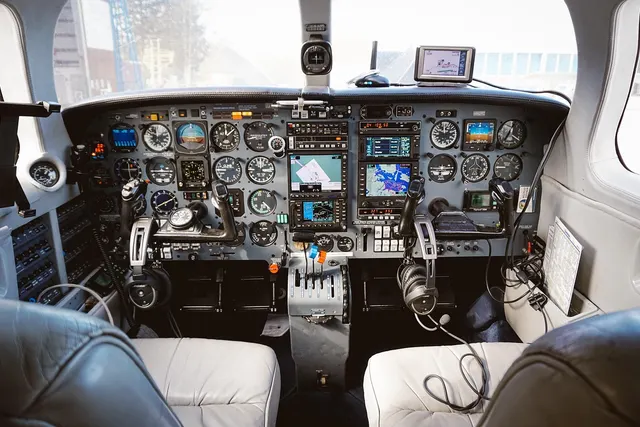 Cockpit of a small private aircraft with analog gauges, GPS navigation screens, control yokes, headsets and leather seats