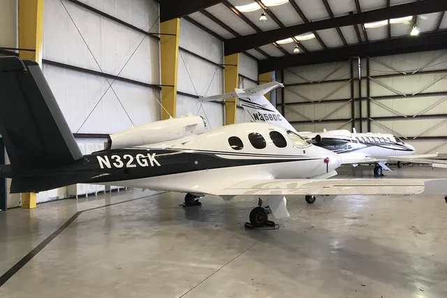 Black and white single-engine private jet parked in a bright hangar beside a larger white business jet