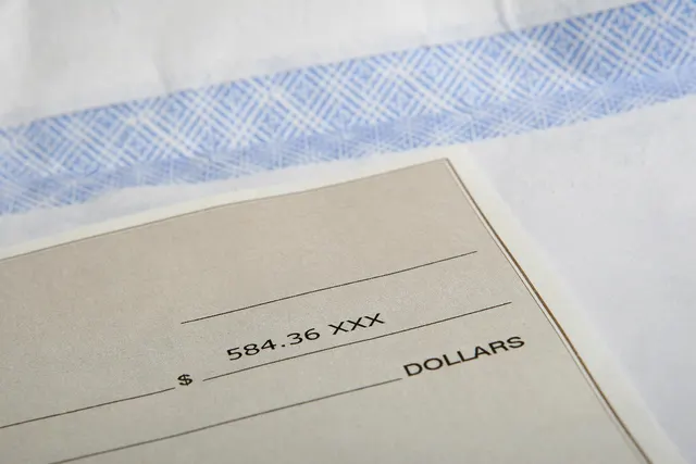 Close-up of a paper check with $584.36 printed on the amount line, resting on a blue-patterned security envelope