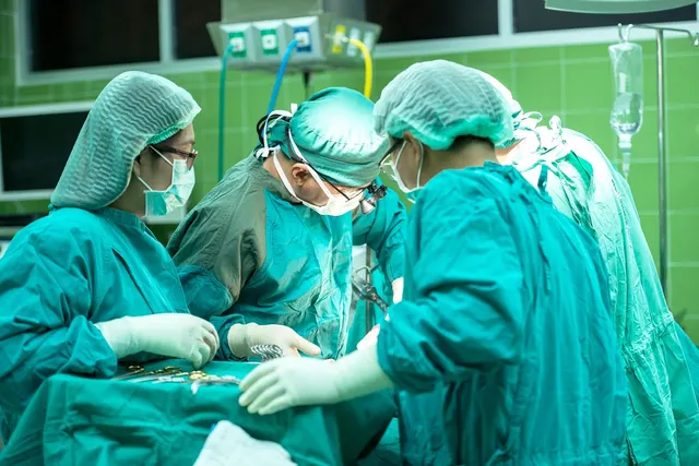 Surgical team in green scrubs, caps and masks performing an operation in a hospital operating room