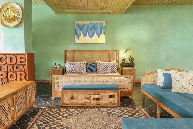 Showroom bedroom with a cane-and-wood bed, blue velvet bench and daybed, mint green walls and a patterned rug