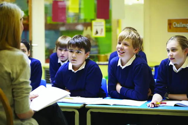 Uniformed schoolchildren sitting at desks, listening to their teacher