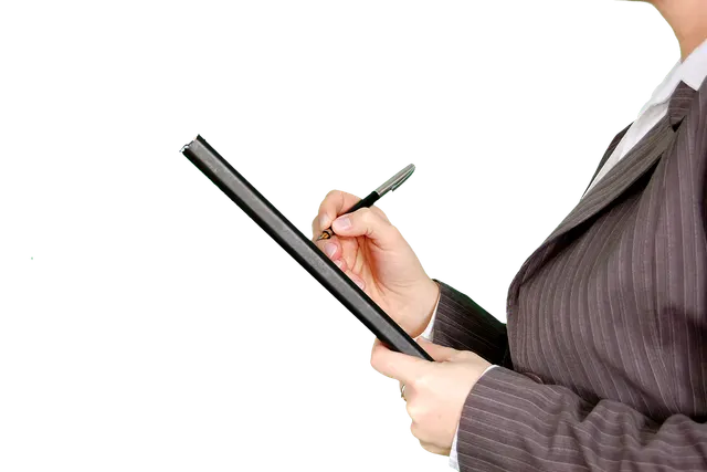 Businesswoman in a gray pinstripe suit writing with a fountain pen on a black clipboard against a black background