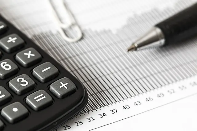 Close-up of a black calculator keypad and silver ballpoint pen resting on a printed financial bar chart report
