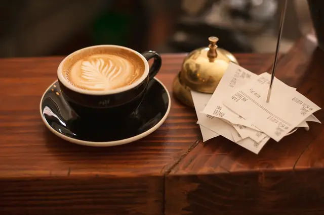 Latte with foam art next to a service bell and receipts on a spike