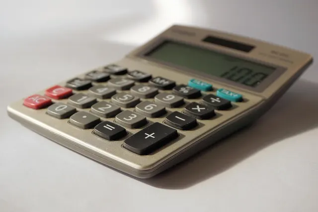 Close-up of a silver desktop calculator with gray, red and teal keys on a white surface, display reading 100