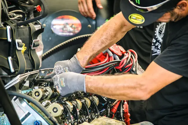 Gloved mechanic repairing a car engine full of wiring