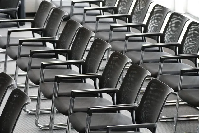 Rows of empty black mesh conference chairs with chrome frames arranged in a bright meeting room