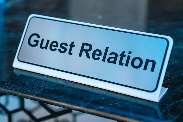 Silver desk sign reading Guest Relation on a dark marble hotel reception counter