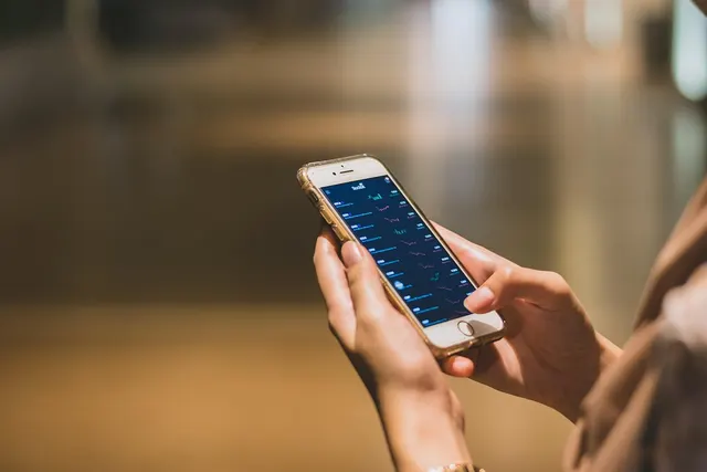 Close-up of hands holding a smartphone displaying a finance app with charts against a blurred background