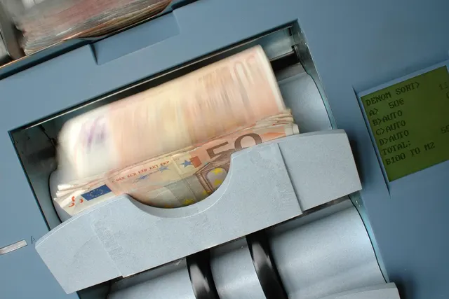 Stack of 50 euro banknotes blurring through a gray cash counting machine with a green LCD display showing denomination sort