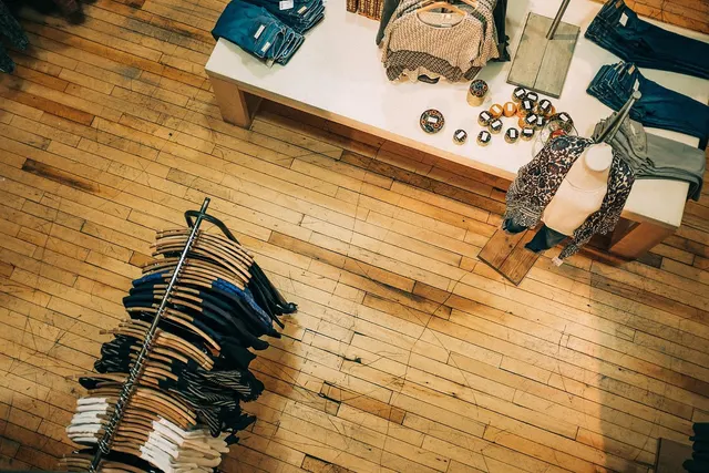 Overhead view of a boutique clothing store with a rack of shirts on wooden hangers and a display table of jeans