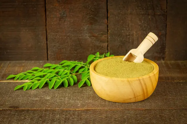 Wooden bowl of fine green powder with a scoop and leaves