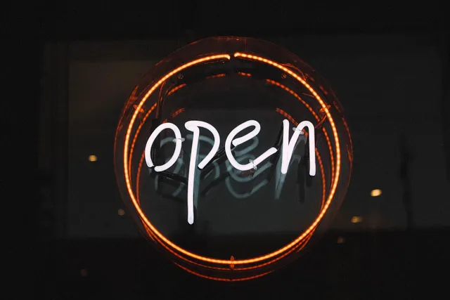 Glowing white neon 'open' sign inside an orange neon circle hanging in a dark shop window at night