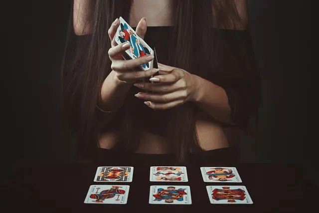 Woman with long dark hair holding a deck of cards above six illustrated cards laid out on a dark table for a reading