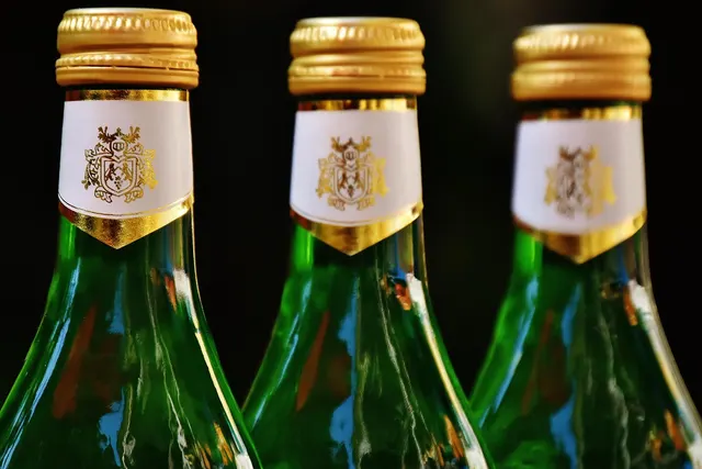 Close-up of three green wine bottle necks with gold screw caps and white neck labels against a dark background