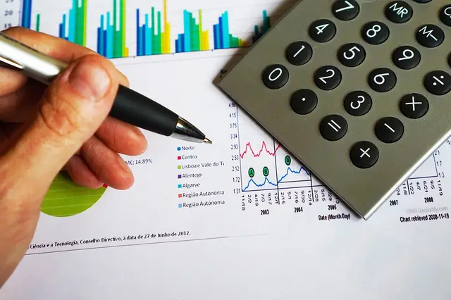 Hand with pen over financial charts next to a calculator