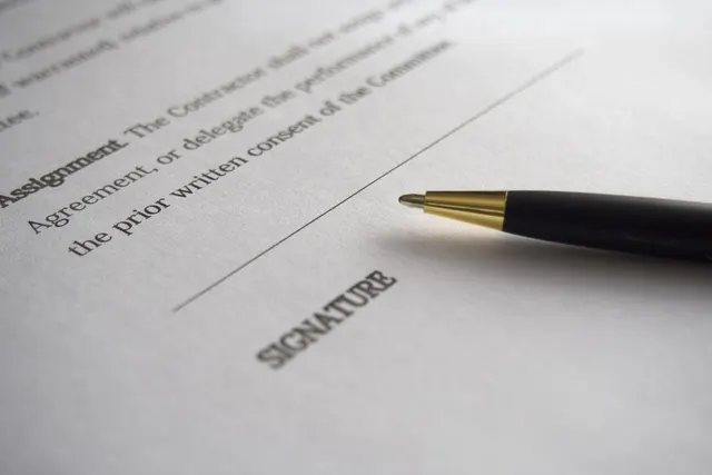Close-up of a black and gold pen resting on a printed contract beside a blank signature line and assignment clause