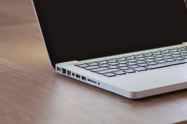 Silver laptop with a dark screen and backlit keyboard sitting open on a light wooden desk