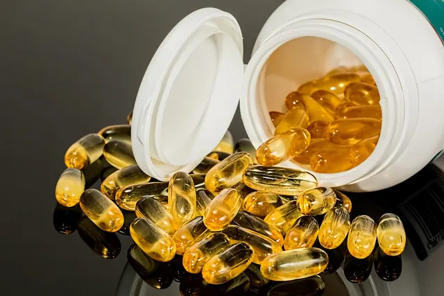 Amber softgel supplement capsules spilling from an open white bottle onto a glossy dark surface