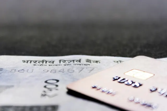 Close-up of a rose-gold EMV chip card with embossed numbers resting on an Indian 100-rupee banknote