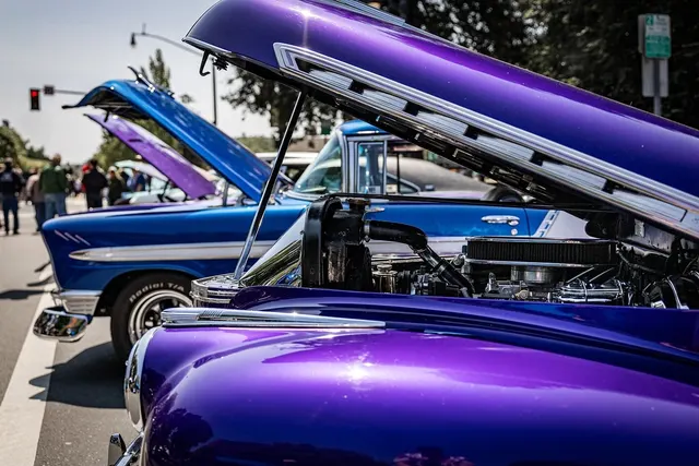 Purple and blue classic cars with raised hoods and chrome engines lined up at an outdoor street car show