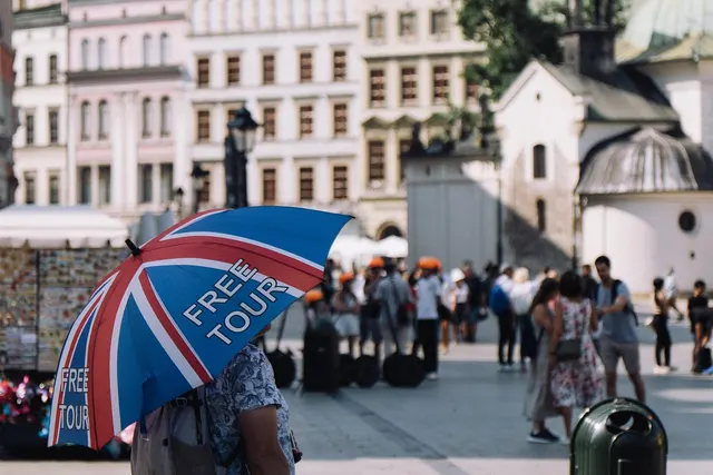 Guide holds a Union Jack umbrella printed with FREE TOUR as tourists gather in a sunny European old town square