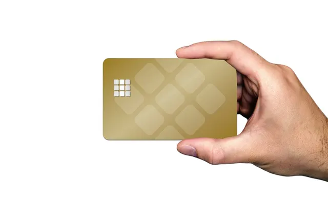 Hand holding a blank gold chip payment card with a diamond pattern against a plain white background