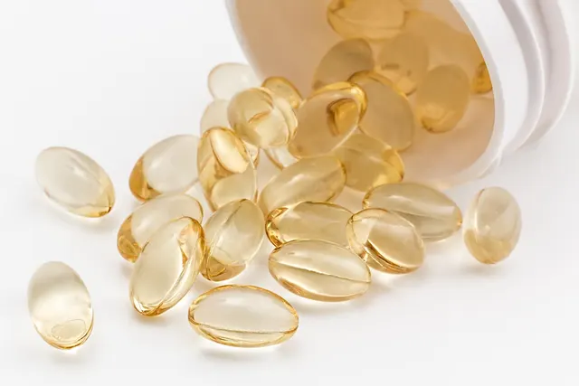 Clear amber softgel supplement capsules spilling from a white plastic bottle onto a white surface