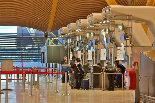Travelers with rolling luggage at airport check-in counters beneath a curved wooden ceiling with overhead displays