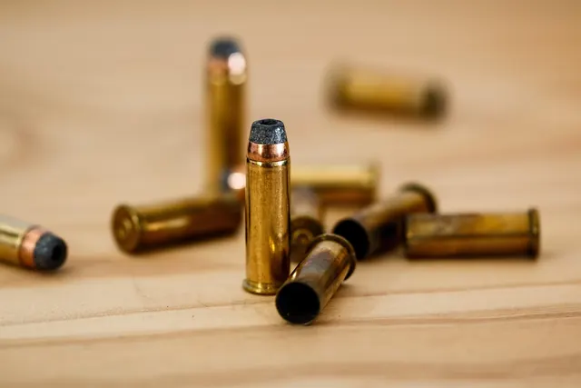 Brass revolver cartridges and spent shell casings scattered on a light wooden table, one round standing upright
