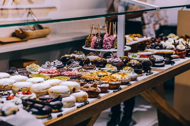 Bakery display counter with rows of glazed and frosted donuts, cake pops and cupcakes behind a glass case