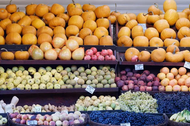 Grocery produce stand with shelves of pumpkins, quinces, pomegranates, persimmons, grapes and bananas with price cards
