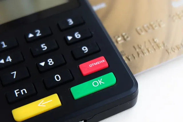 Close-up of a black card payment terminal keypad with green OK and red cancel keys beside a gold credit card