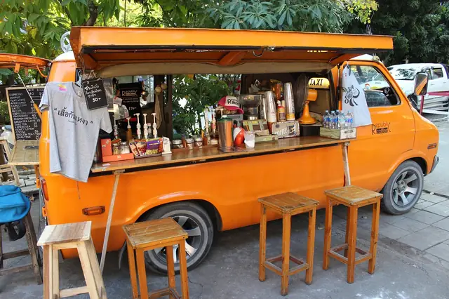 Orange van converted into a coffee stand with wooden stools