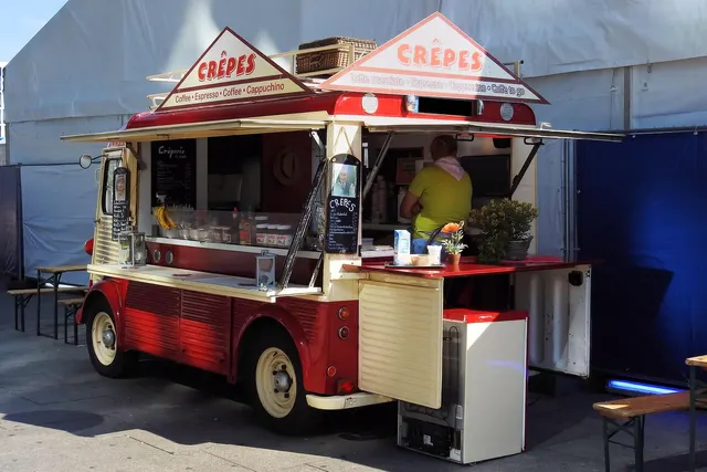 Vintage red and cream crêpe van with an open service window and a vendor in a yellow shirt preparing orders inside
