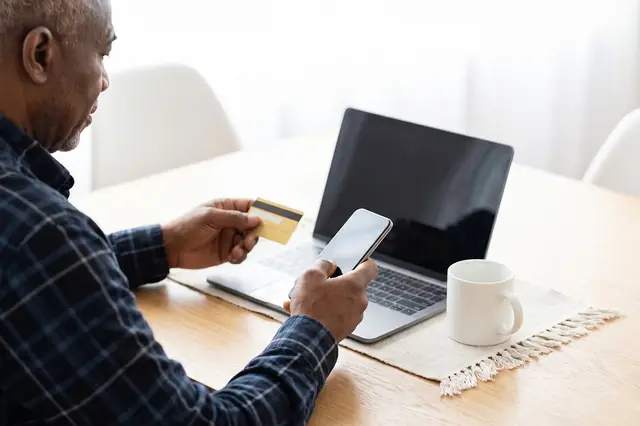 Man holding a card and smartphone in front of a laptop