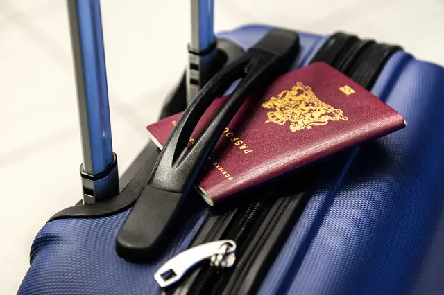 Passport tucked into the handle of a blue suitcase