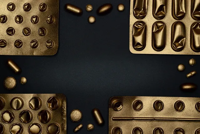 Gold-toned blister packs, some with empty popped pockets, and loose pills and capsules arranged on a dark background