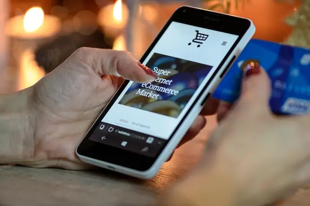 Hand holding a smartphone with a shopping app and a card