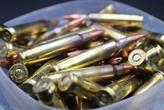Close-up of brass rifle cartridges with copper-tipped bullets piled in a clear plastic container