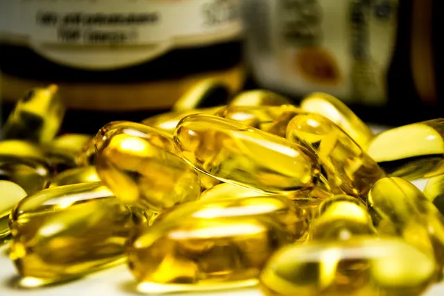 Close-up of golden fish oil softgel capsules piled on a white surface with blurred supplement bottles behind
