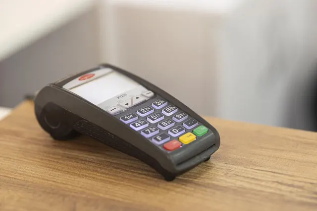 Black card payment terminal with a numeric keypad and small display resting on a wooden counter