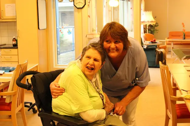 Caregiver hugging a smiling elderly woman in a wheelchair