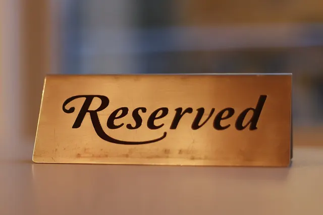 Brass tabletop sign engraved with the word Reserved in script lettering, set on a table against a softly blurred background
