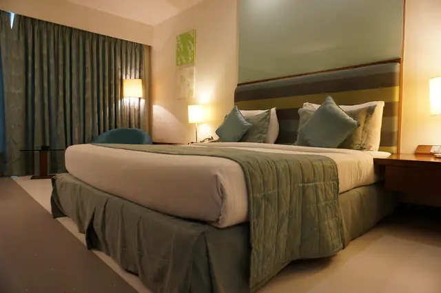 Neatly made hotel bed with green throw and pillows
