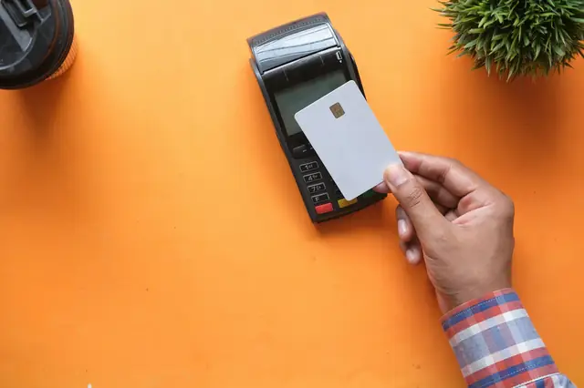 Customer holding a card beside a payment terminal on an orange counter