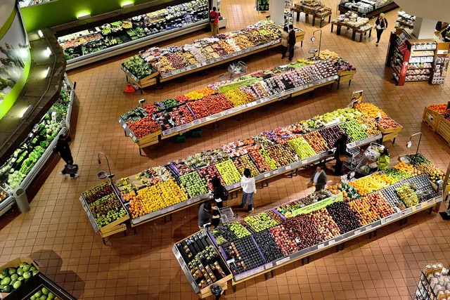 Overhead view of a grocery store produce section with long displays of fresh fruits and vegetables and shoppers with carts