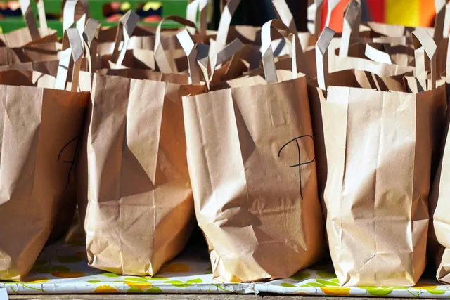 Rows of filled brown paper grocery bags with handles lined up on a table, ready for customer pickup