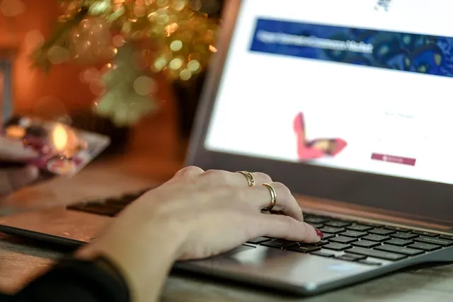 Woman's ringed hand typing on a laptop showing an online shoe store while holding a credit card in her other hand